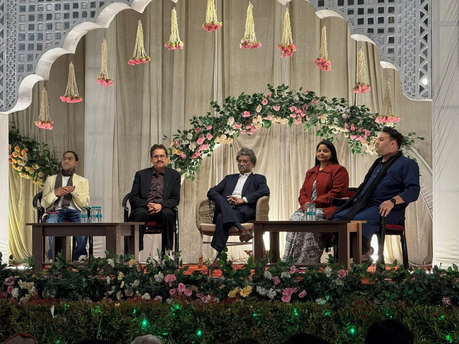 Speakers seated on a decorated stage during a poetry event at Adarsh Vatika