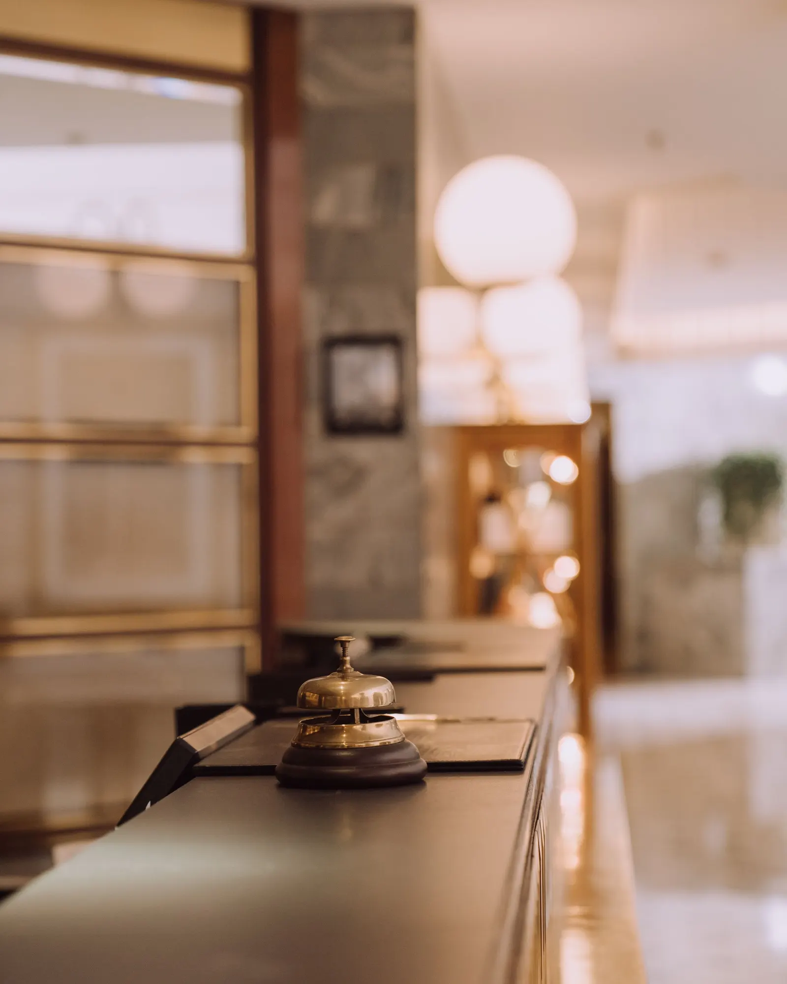 Temporary concept image of a brass bell on a wooden reception counter under warm lamplight; not property photography.