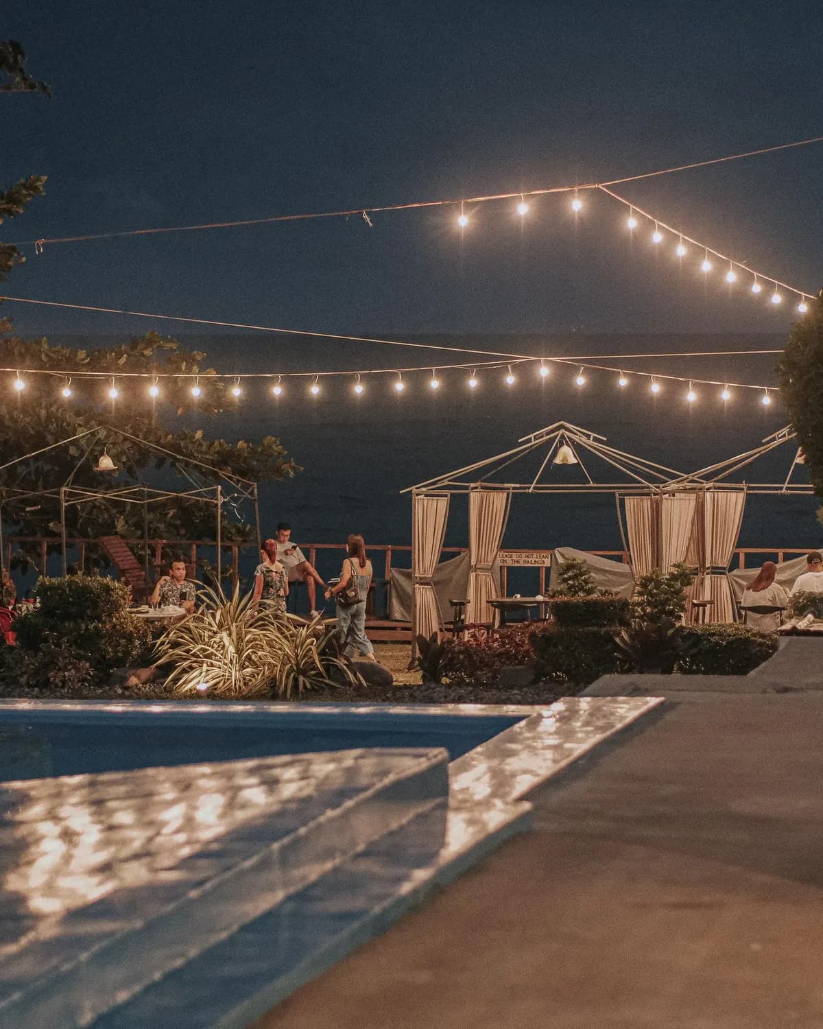 Temporary concept image of friends gathered beside a pool in the evening under string lights; not property photography.