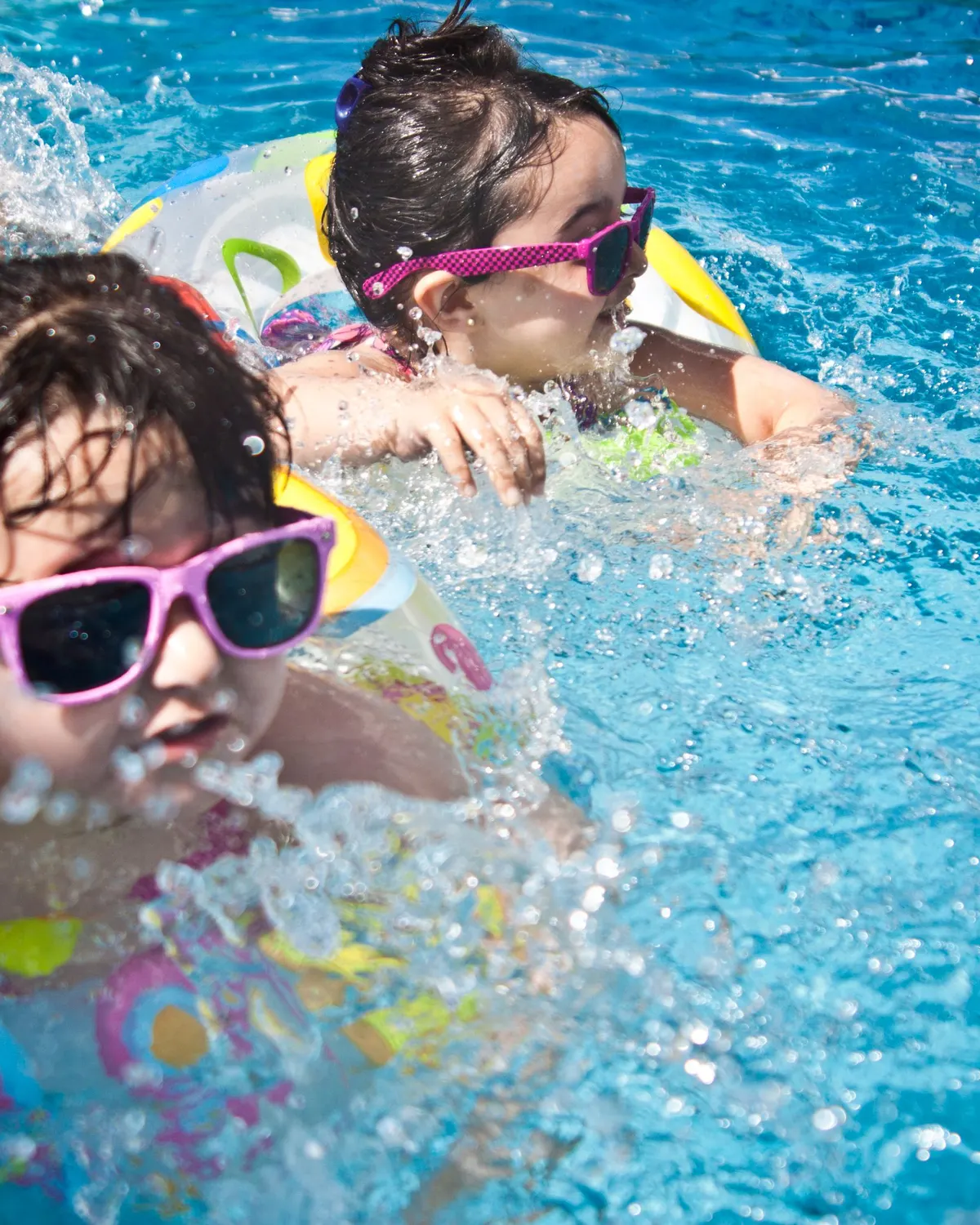 Temporary concept image of children playing happily with float rings in clear pool water; not property photography.