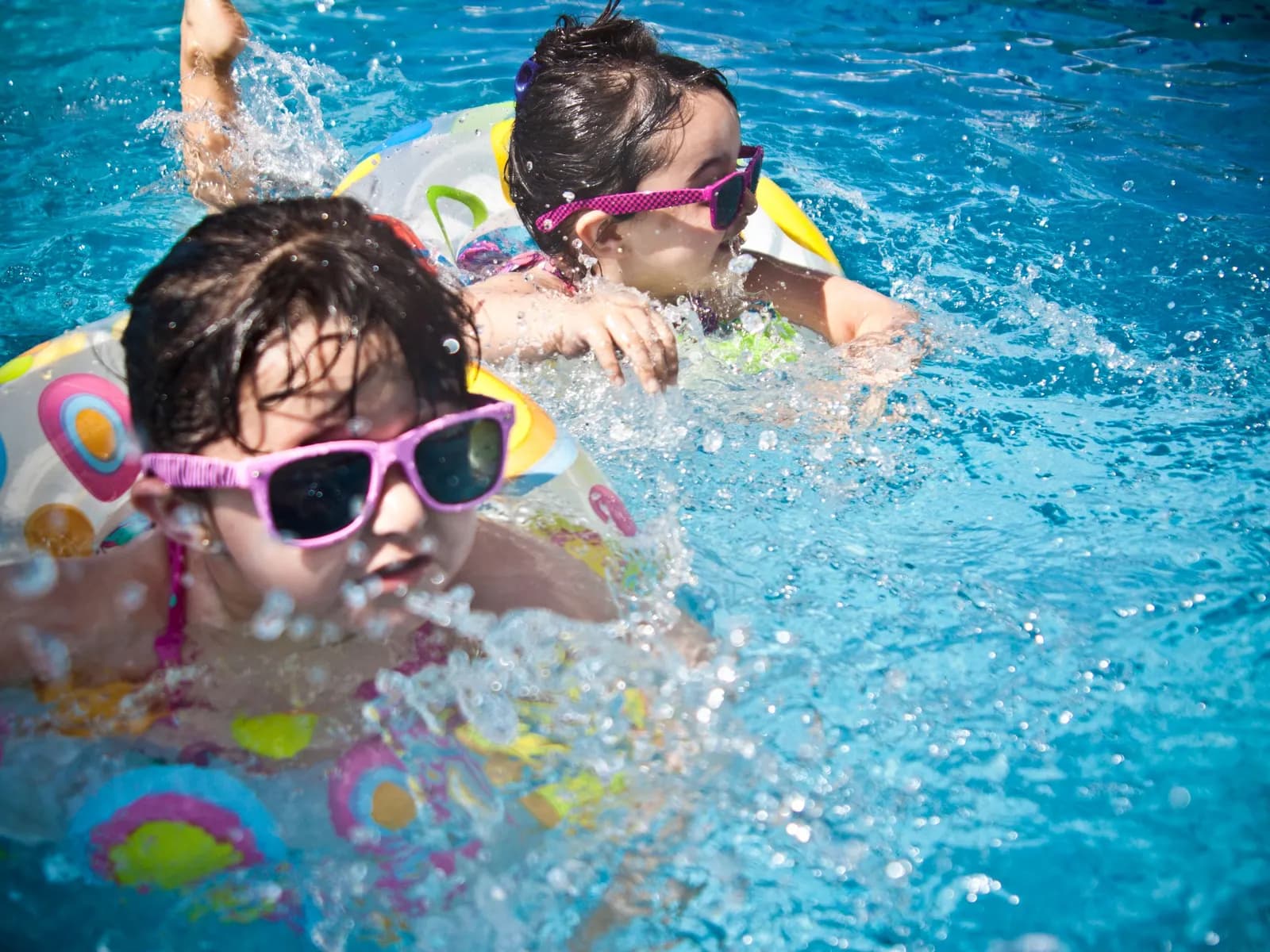 Temporary concept image of children playing happily with float rings in clear pool water; not property photography.