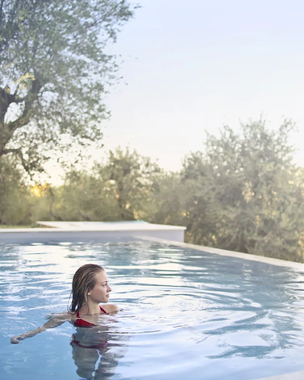 Temporary concept image of a swimmer gliding through an outdoor pool edged by greenery; not property photography.