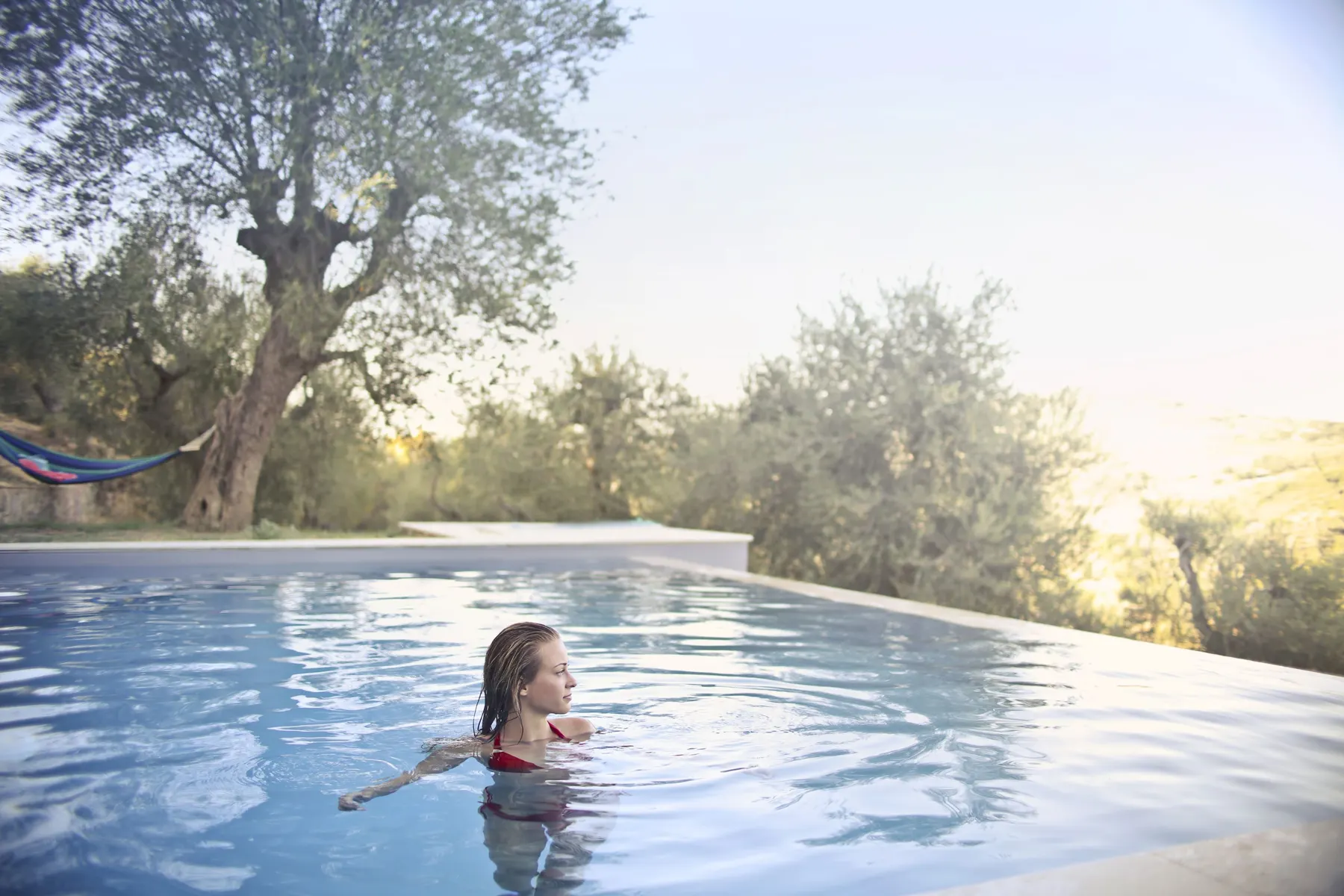 Temporary concept image of a swimmer gliding through an outdoor pool edged by greenery; not property photography.