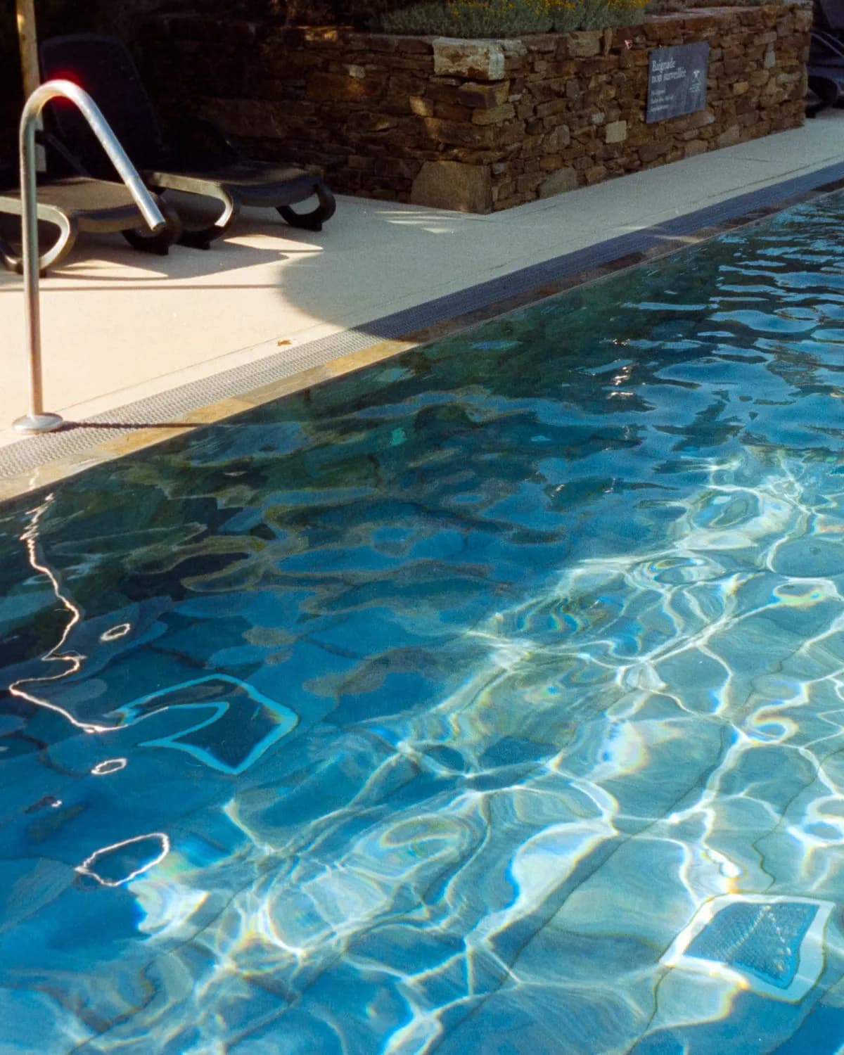 Temporary concept image of sunlit pool with empty loungers waiting at its edge; not property photography.