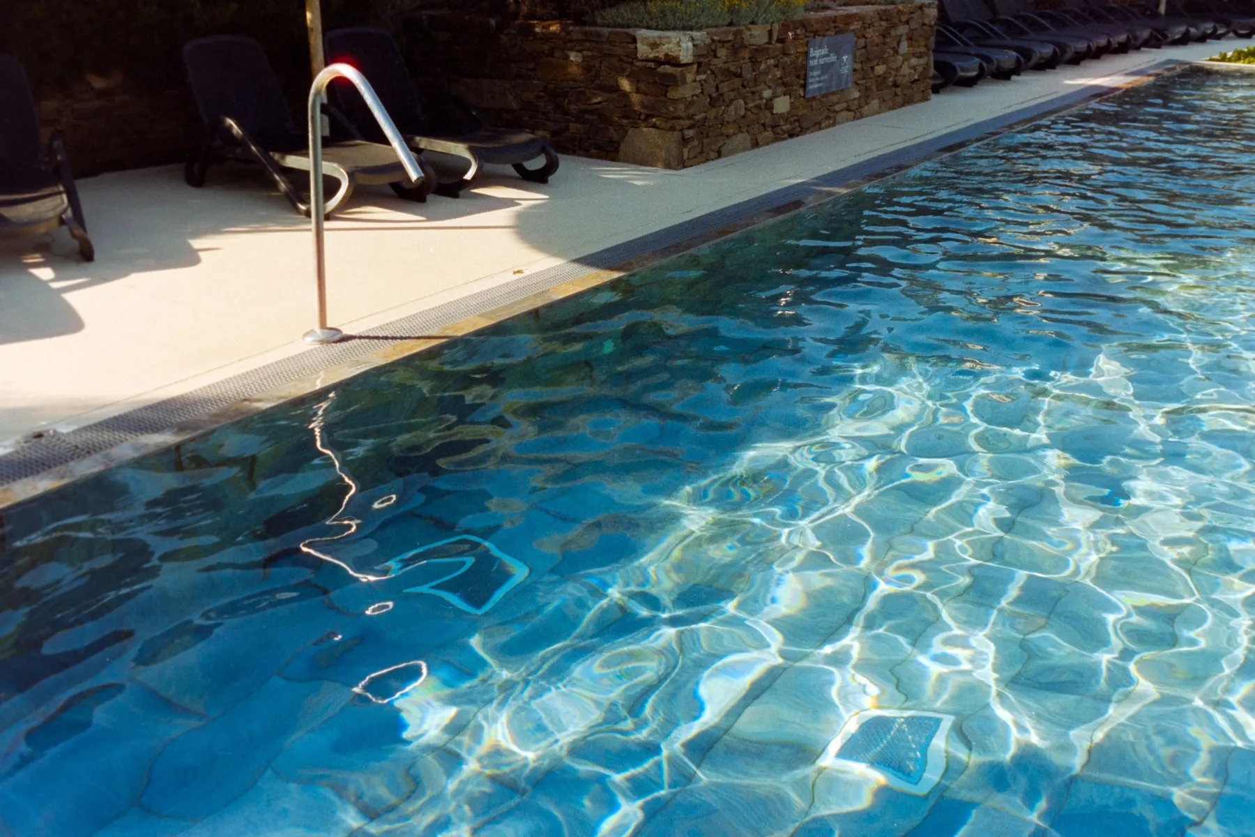 Temporary concept image of sunlit pool with empty loungers waiting at its edge; not property photography.