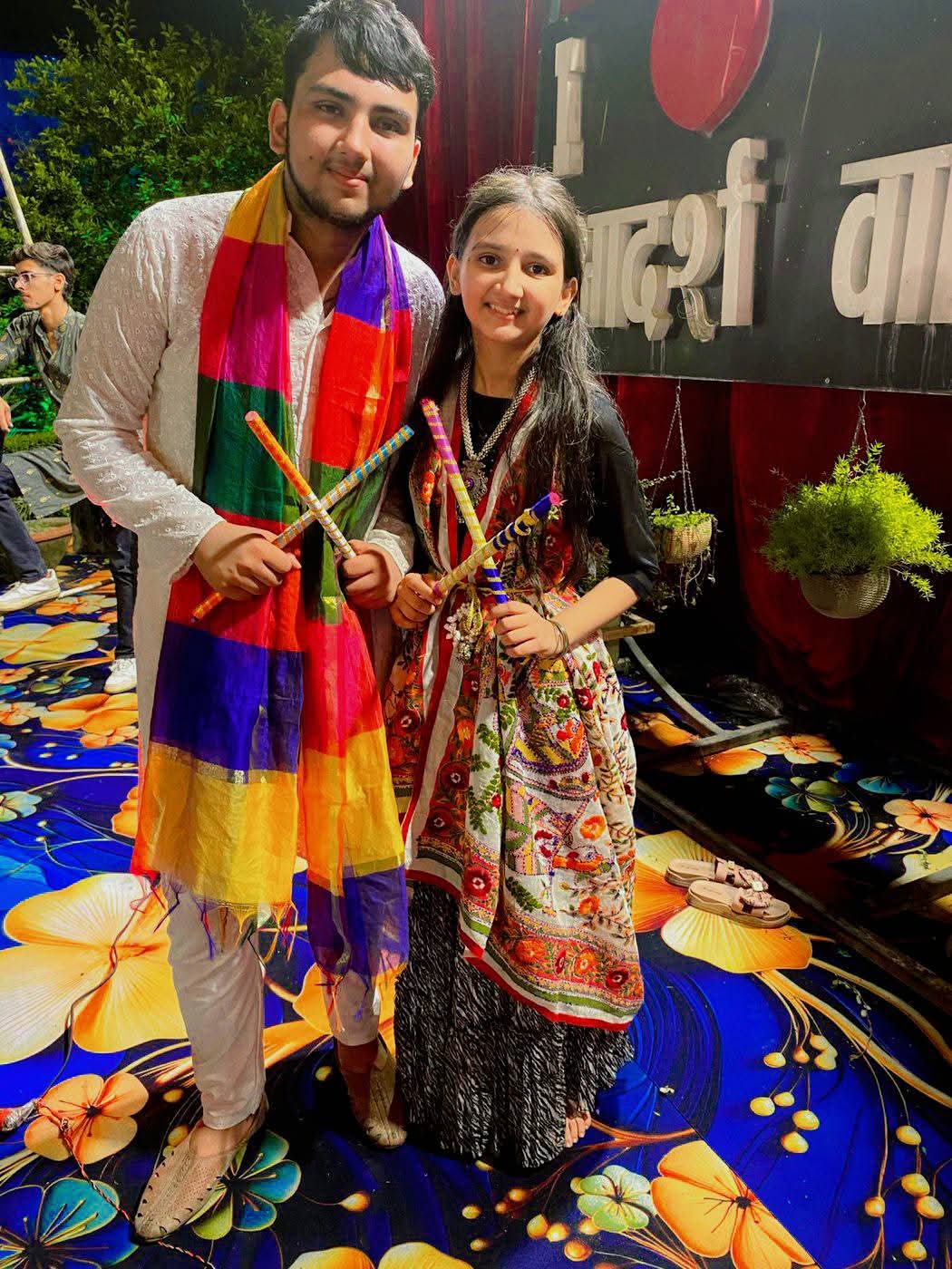 Two young guests holding decorated dandiya sticks at a festive event