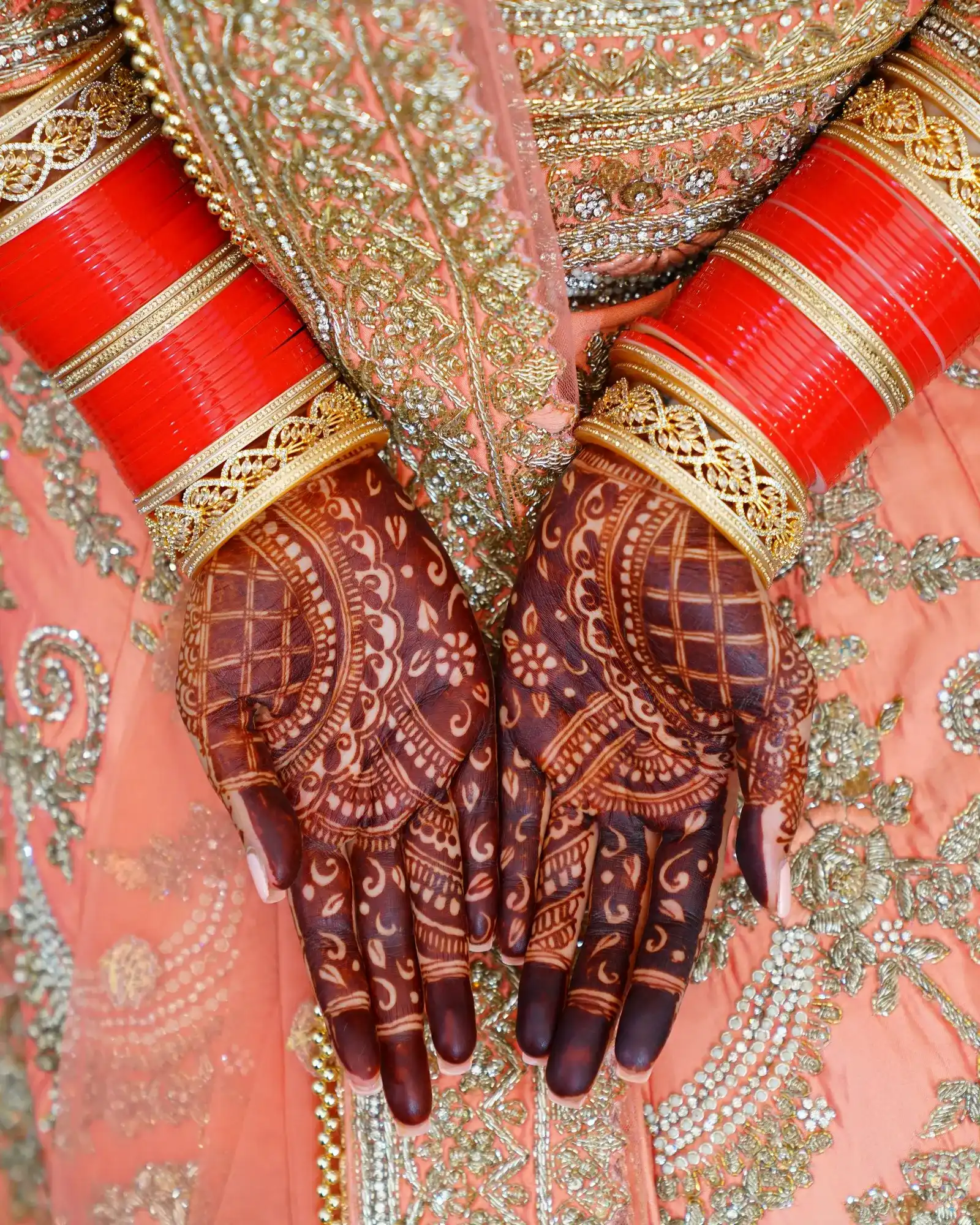 Temporary concept image of henna-covered hands with red bangles seen from above; not property photography.