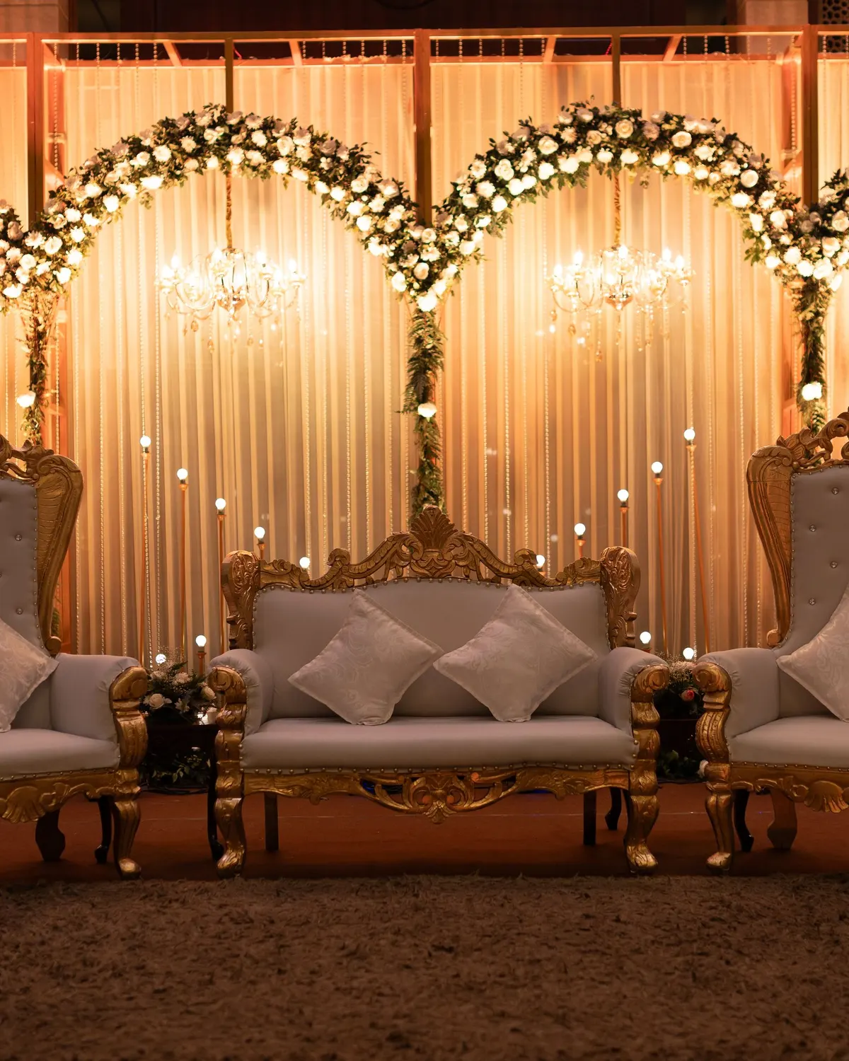 Temporary concept image of reception stage with ornate chairs and floral arrangements under warm lighting; not property photography.