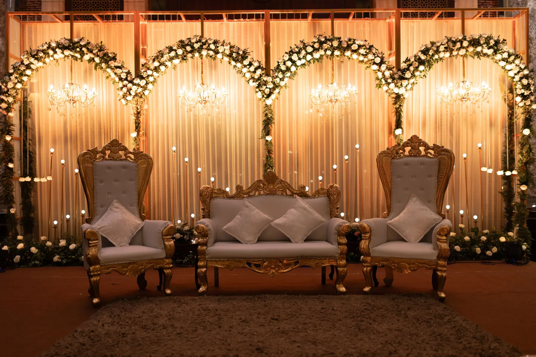 Temporary concept image of reception stage with ornate chairs and floral arrangements under warm lighting; not property photography.