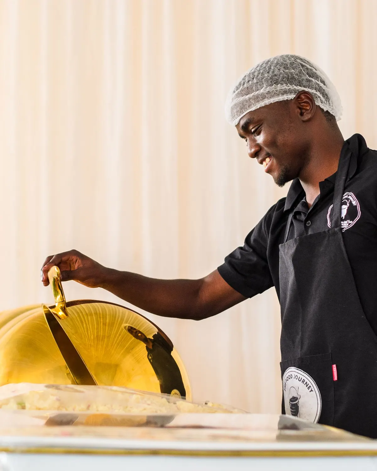Temporary concept image of a chef lifting a gold cloche at a buffet service station; not property photography.