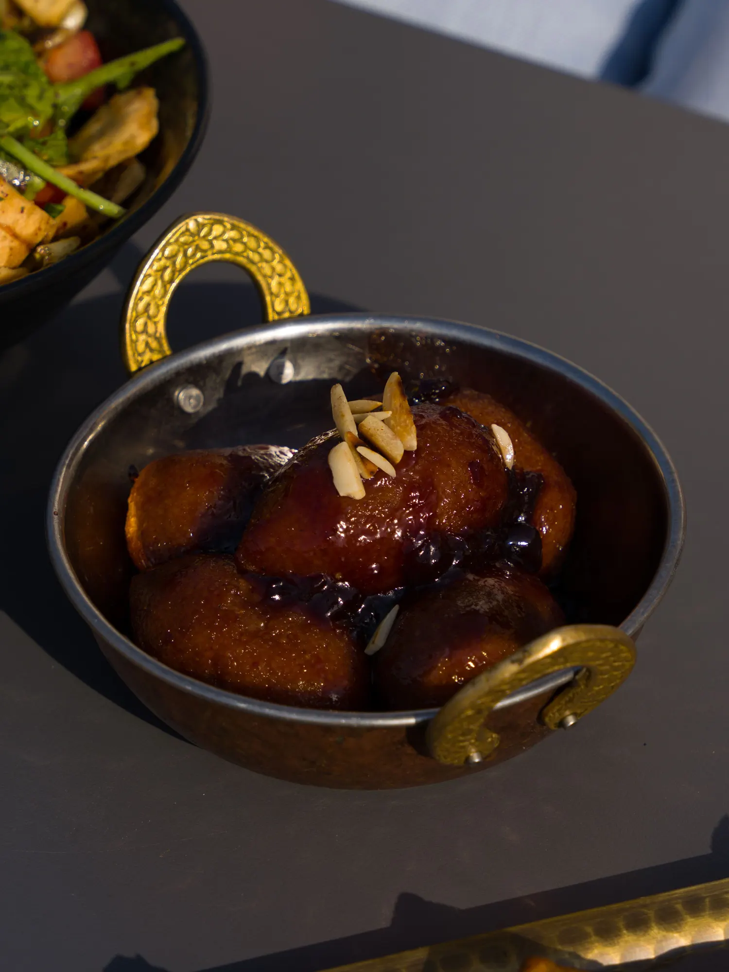 Temporary concept image of gulab jamun garnished with almonds in a serving bowl; not property photography.