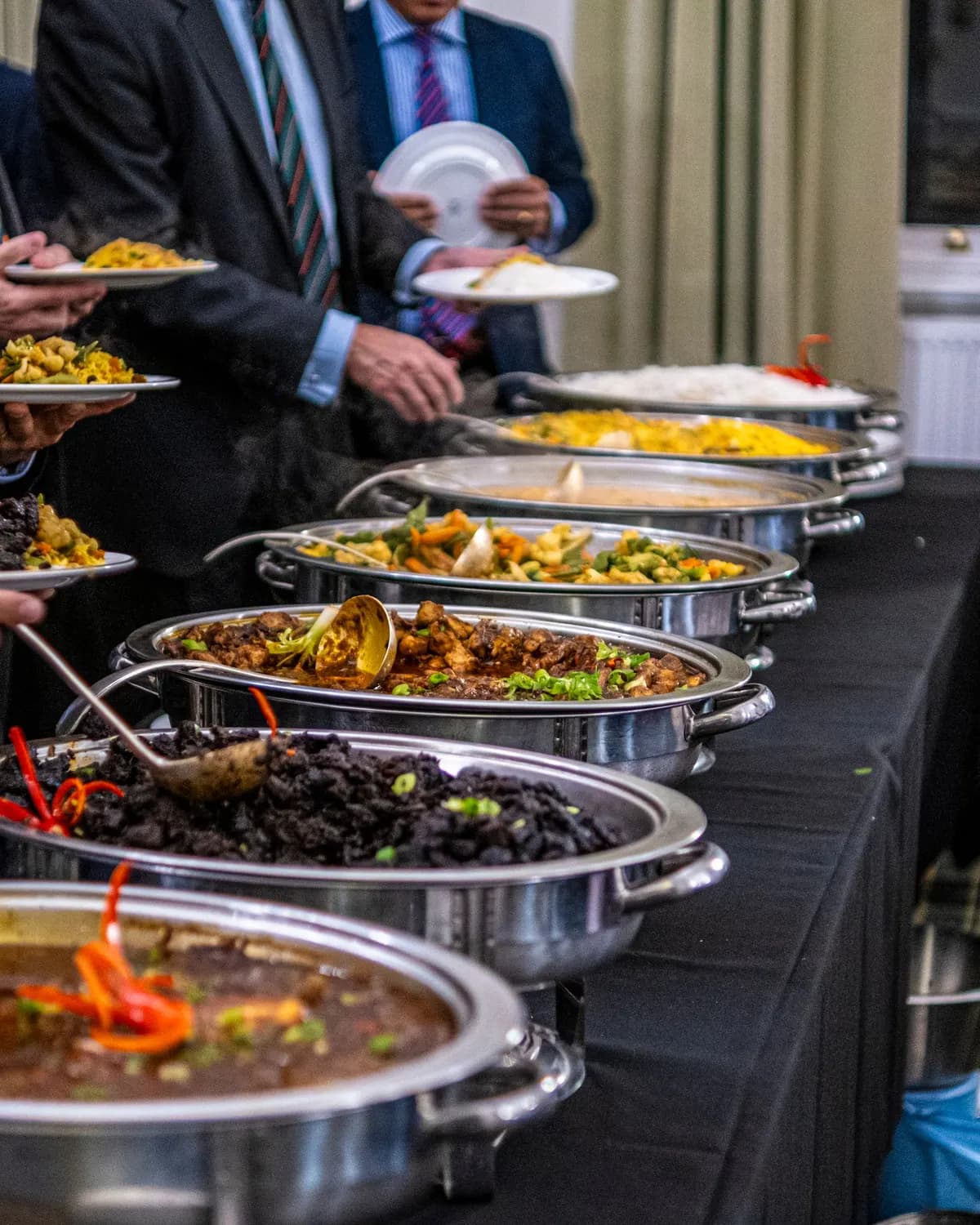 Temporary concept image of colleagues in formal wear serving themselves from a working-lunch buffet; not property photography.