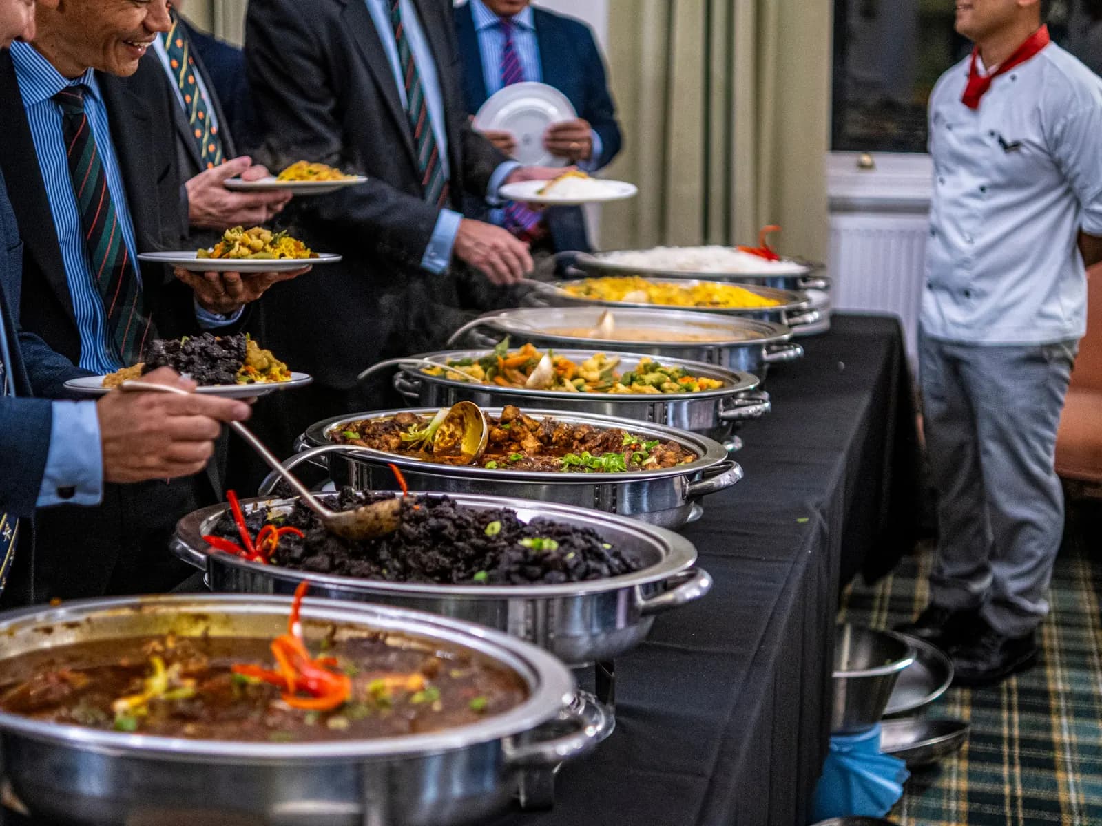 Temporary concept image of colleagues in formal wear serving themselves from a working-lunch buffet; not property photography.