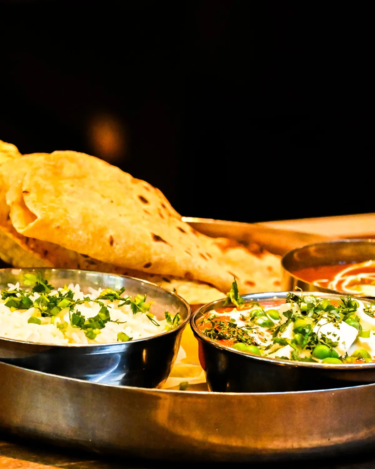 Temporary concept image of indian thali with naan, curries and rice served on a wooden table; not property photography.