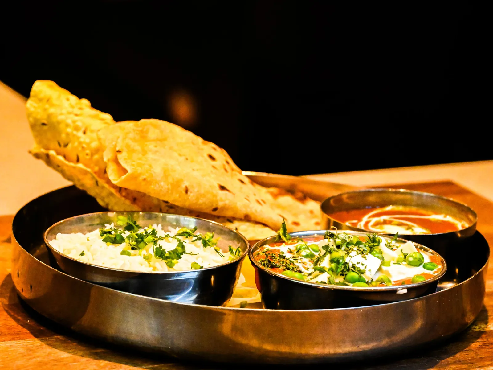 Temporary concept image of indian thali with naan, curries and rice served on a wooden table; not property photography.