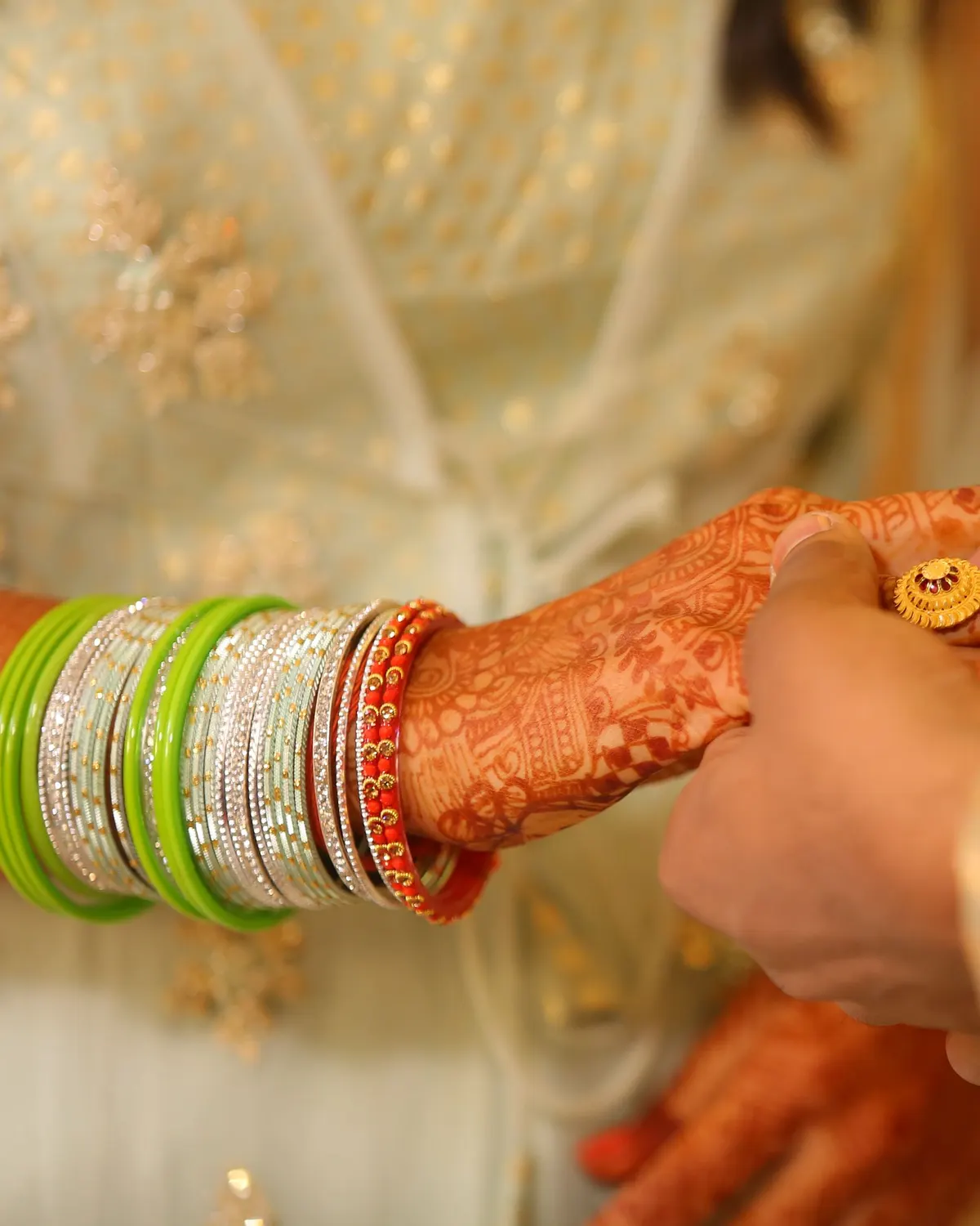Temporary concept image of a gold ring held between henna-decorated hands during a ring ceremony; not property photography.