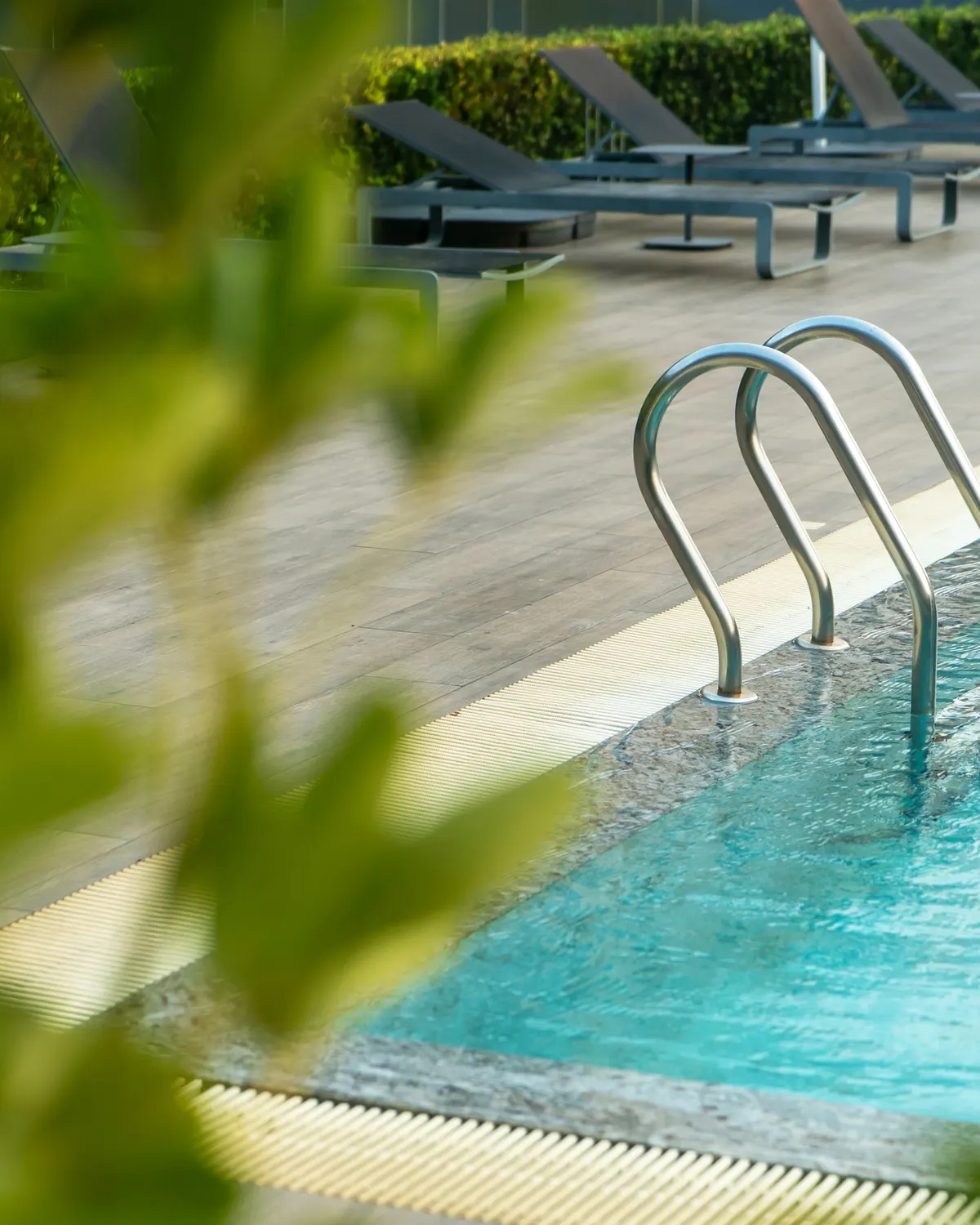 Temporary concept image of open-air swimming pool bordered by loungers and greenery in daylight; not property photography.