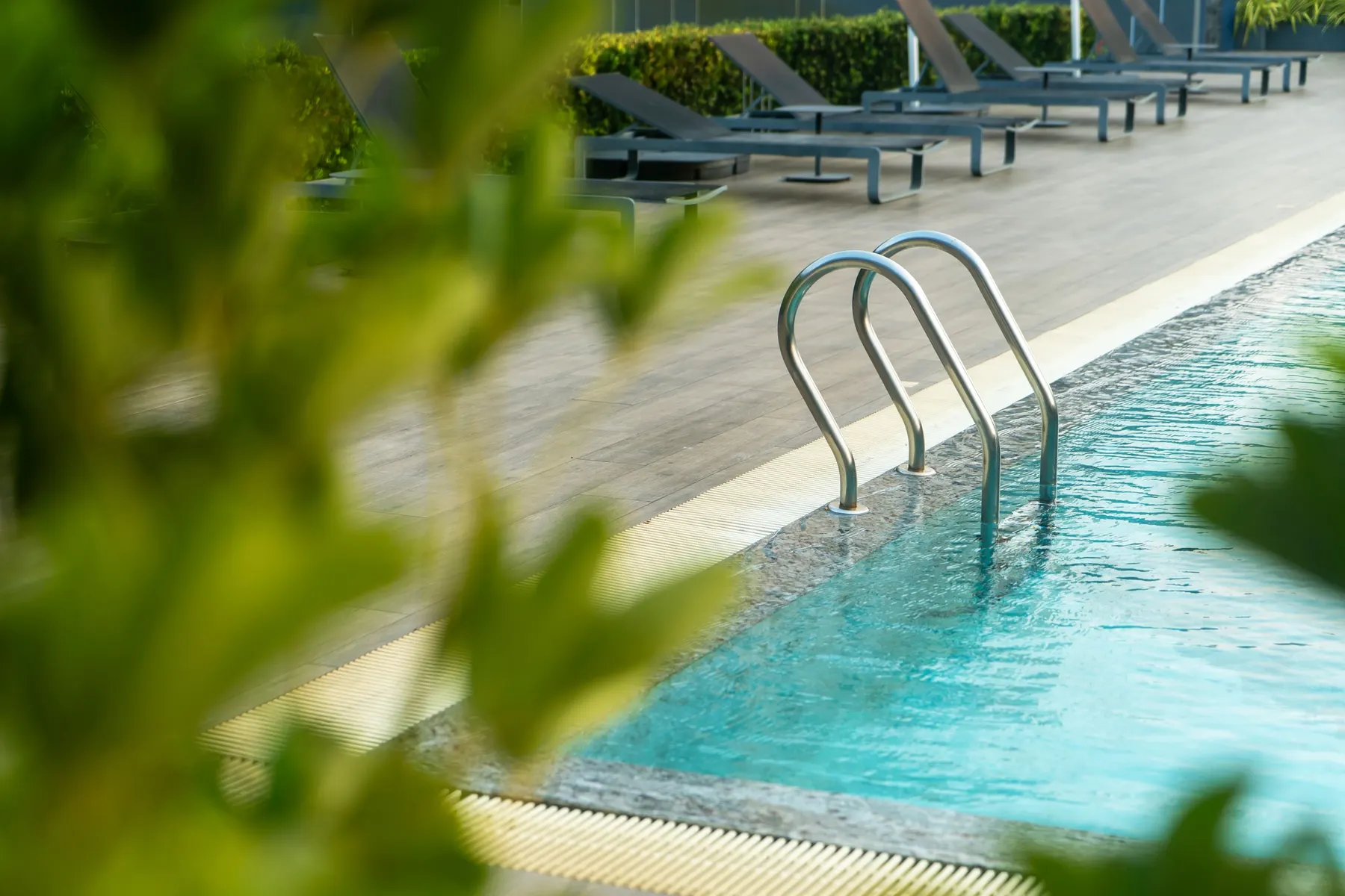 Temporary concept image of open-air swimming pool bordered by loungers and greenery in daylight; not property photography.