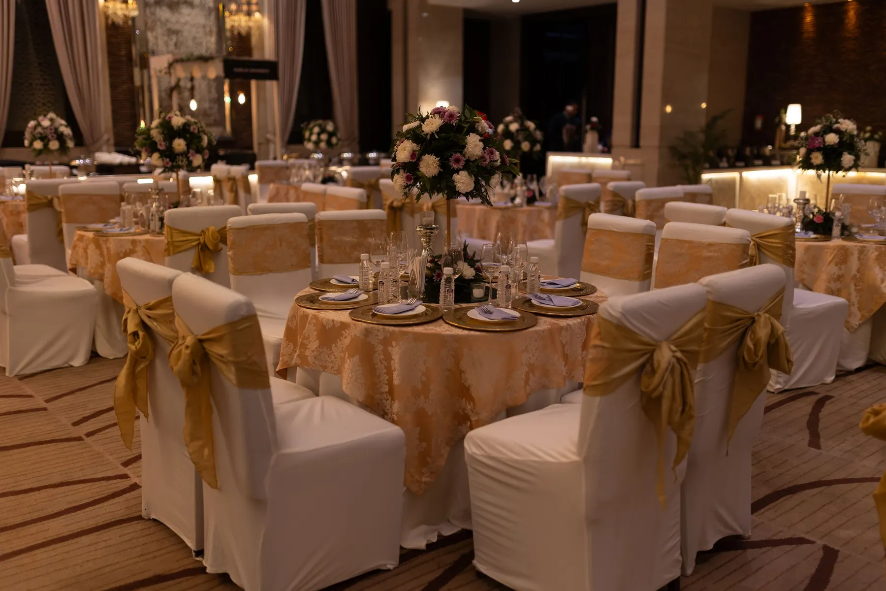 Temporary concept image of banquet tables dressed in ivory and gold with floral centrepieces under warm light; not property photography.