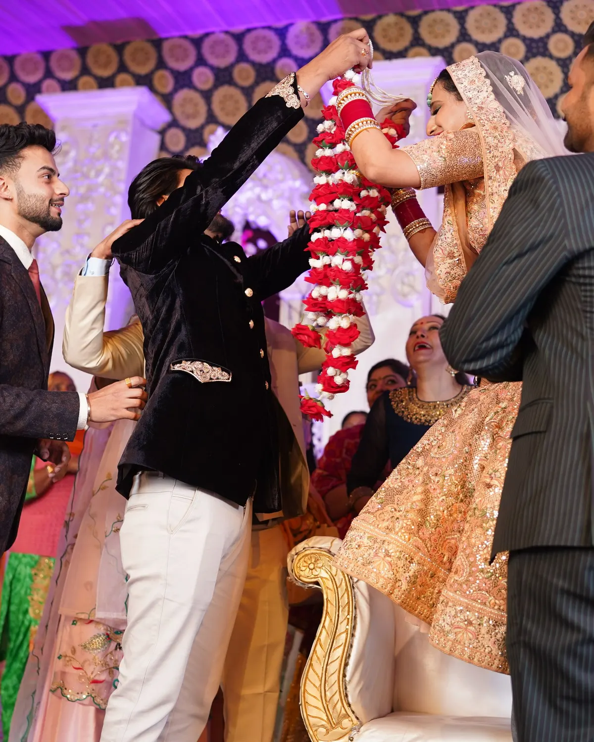 Temporary concept image of bride and groom exchanging garlands amid family celebration; not property photography.