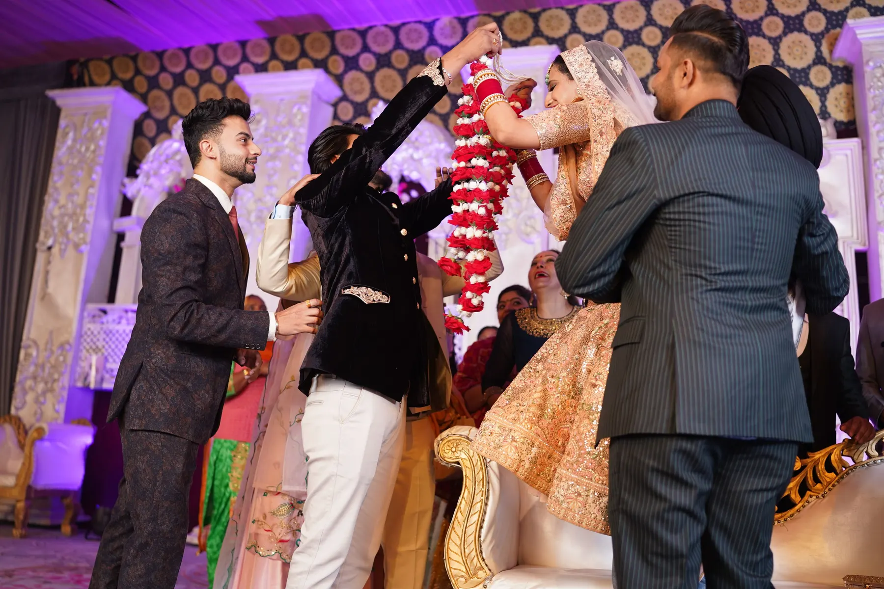 Temporary concept image of bride and groom exchanging garlands amid family celebration; not property photography.