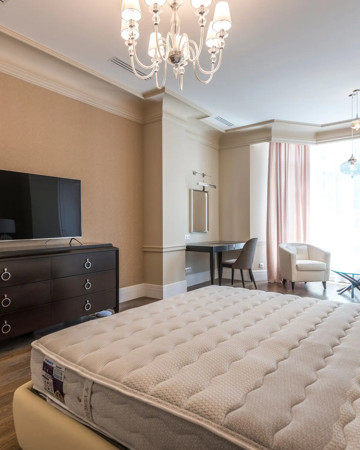 Temporary concept image of spacious bedroom with upholstered headboard and a soft chandelier; not property photography.