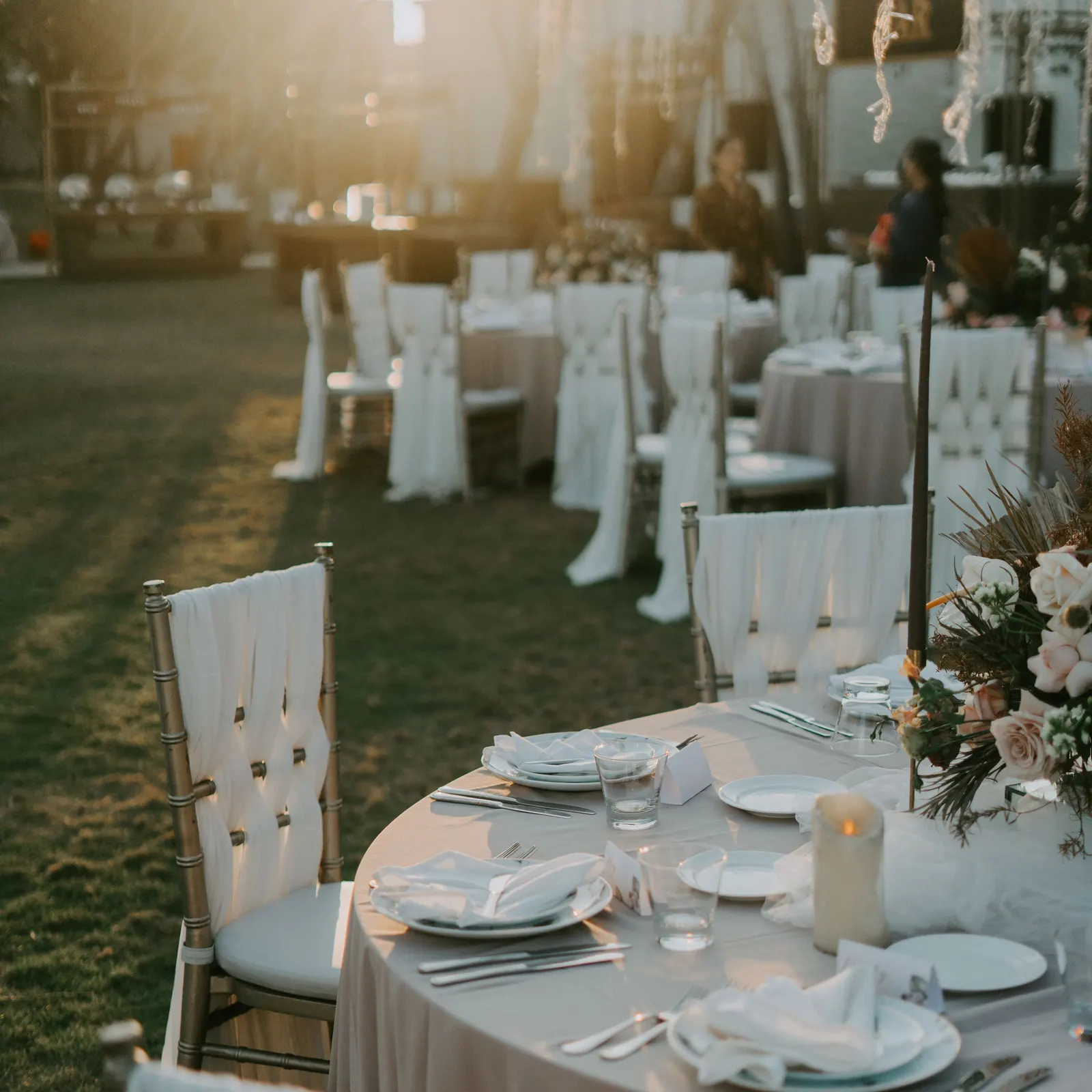 Temporary concept image of lawn dinner tables dressed in white as evening light settles; not property photography.